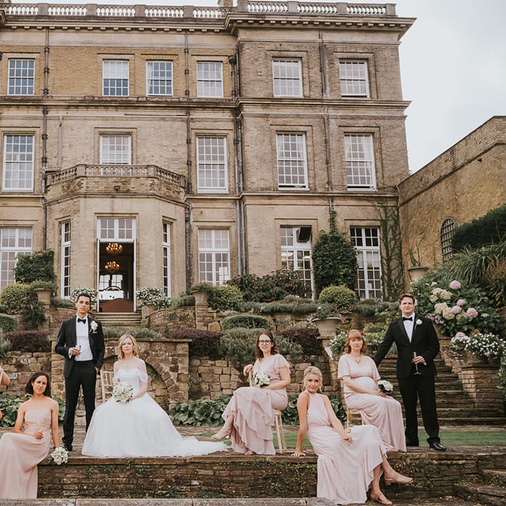 Wedding party shot of groom, groomsmen, bridesmaids and bride in front of country house venue 