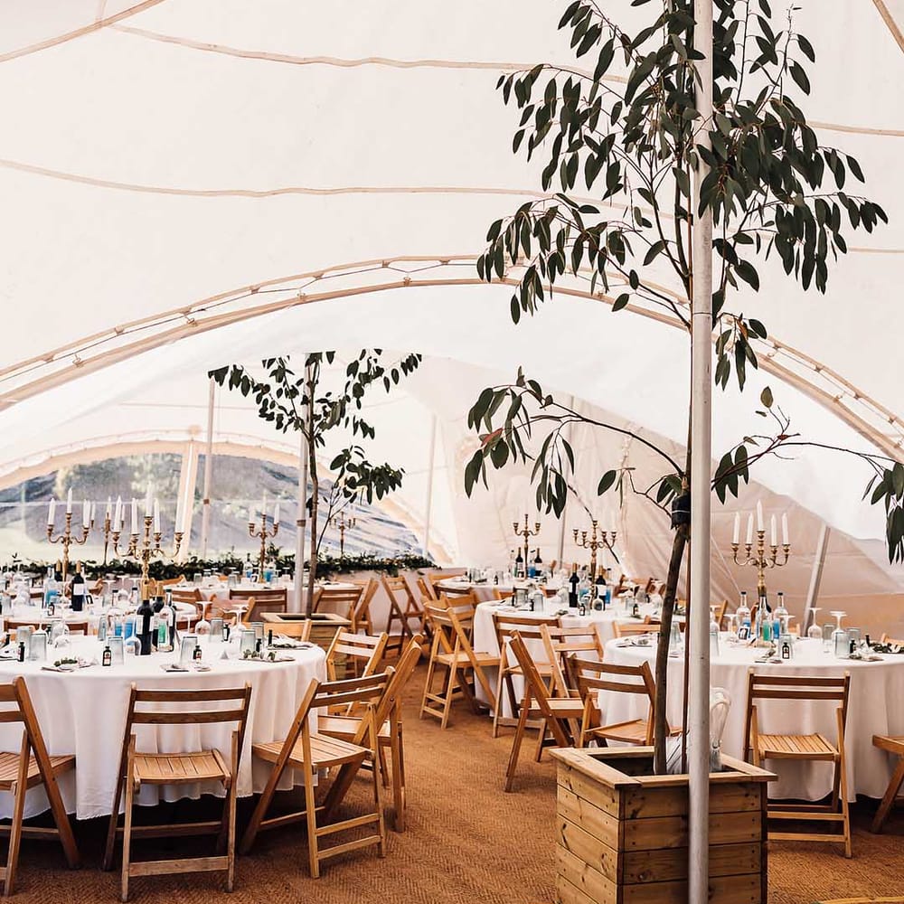 Marquee with circular tables with white wooden chairs and candelabra centrepieces with greenery 