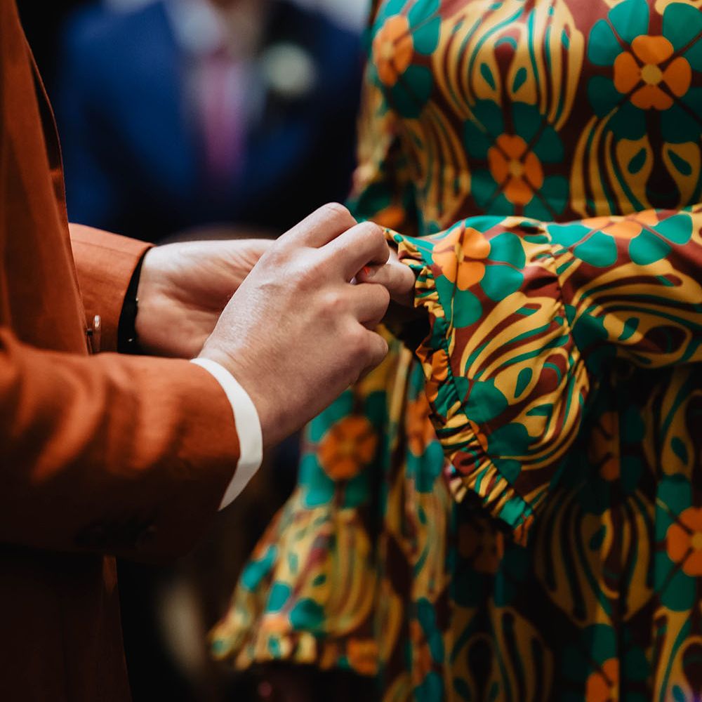 Groom places ring on his brides finger who wears brightly coloured wedding gown 
