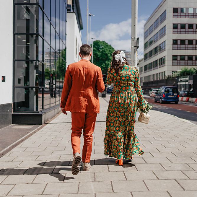 Groom wearing orange linen Paul Smith suit walks with his bride in brightly coloured dress and orange heels 
