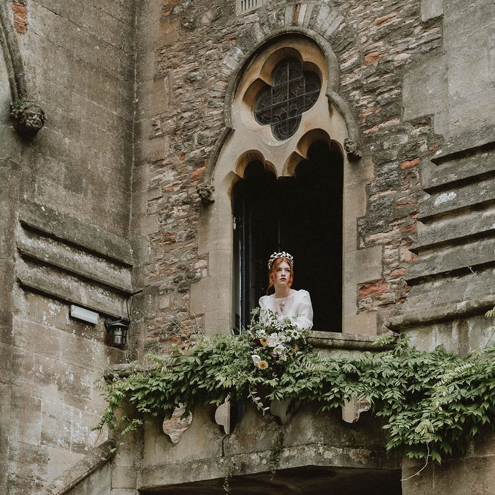 Bride in a gold crown looking over a veranda at Bishop's Palace Wells wedding venue in Somerset 