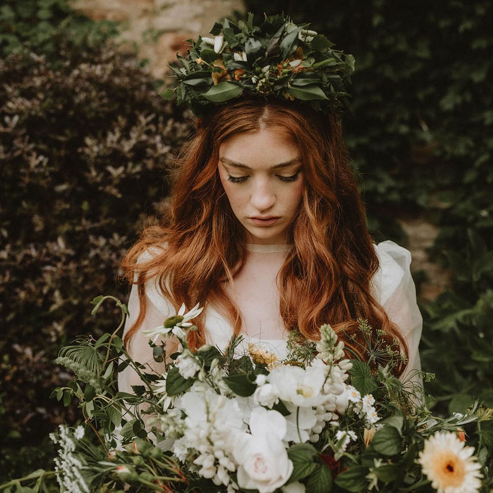 Bride with long wavy red hair and natural wedding makeup wearing a green flower crown holding a giant wedding bouquet 