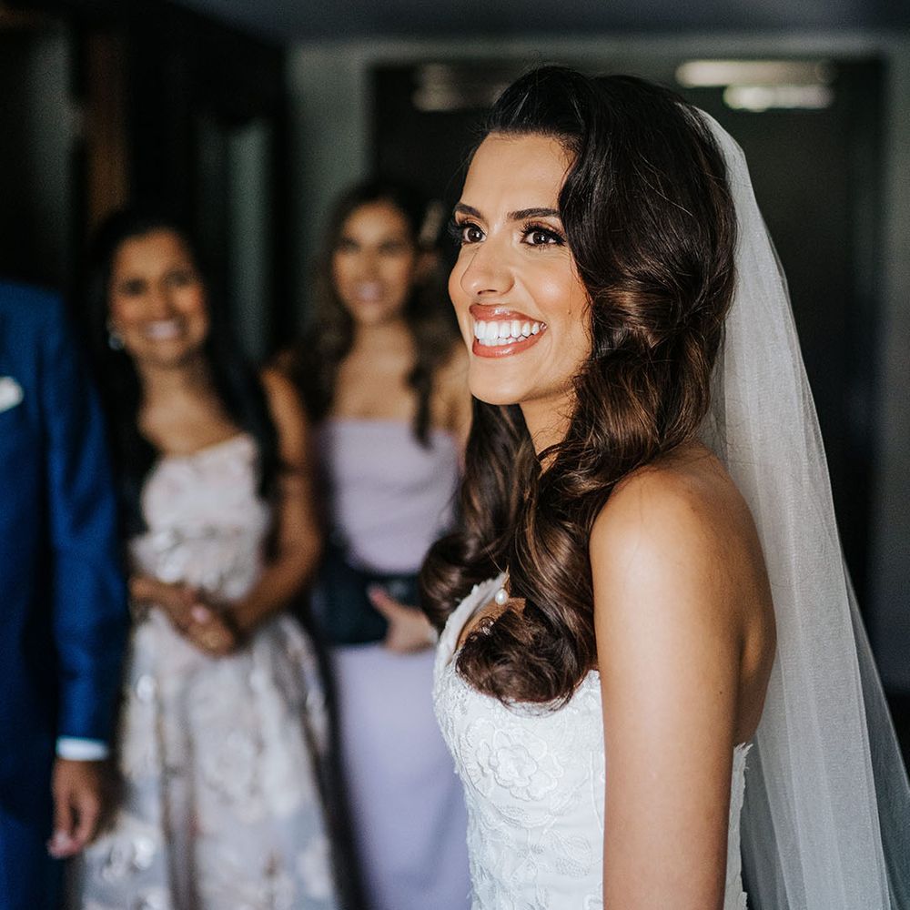 Bride smiles brightly wearing cathedral veil and lace wedding dress on the morning of her wedding day at Syon Park