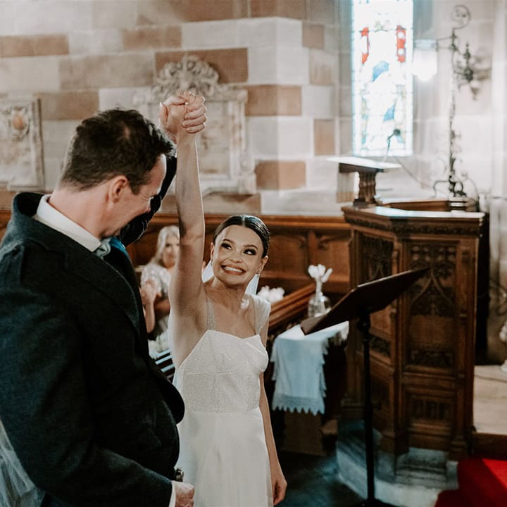 Groom lifts the bride's hand as she beams and they're announced a married couple at their church wedding 