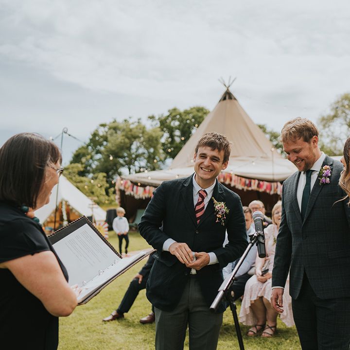 Bride in colourful flower crown stands beside her groom outdoors during wedding ceremony at Burrow Farm Gardens 