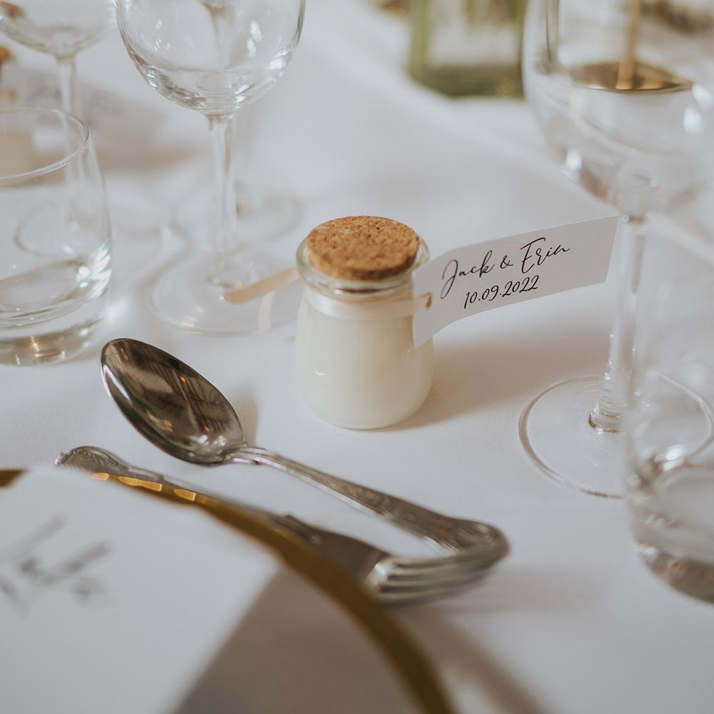 Small glass pot wedding favours with cork lid and personalised label with the date of the wedding and the couple's names 