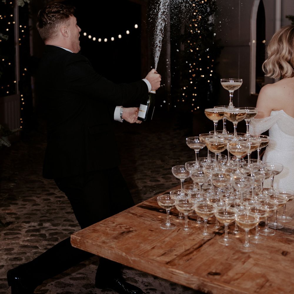The bride reacts to the groom popping open the champagne to pour on their champagne tower 