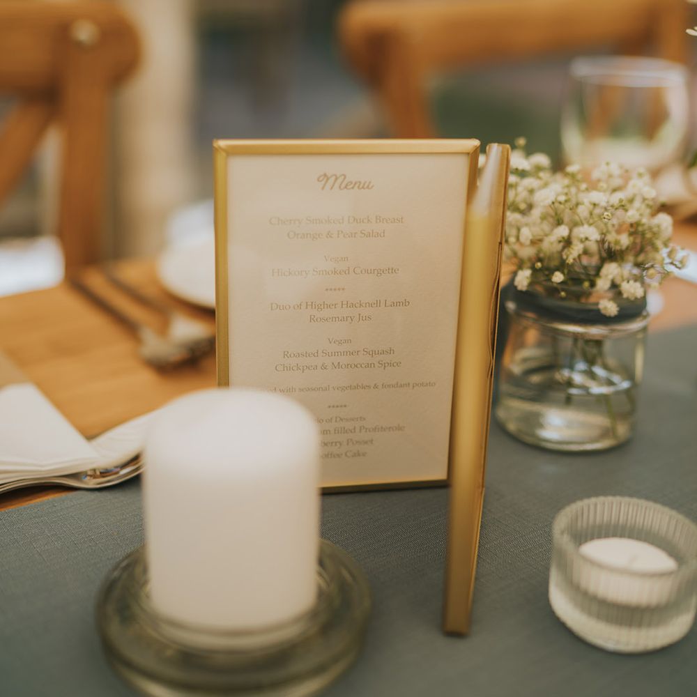 Gold framed wedding menu surrounded by candles at Badgers Holt wedding venue 