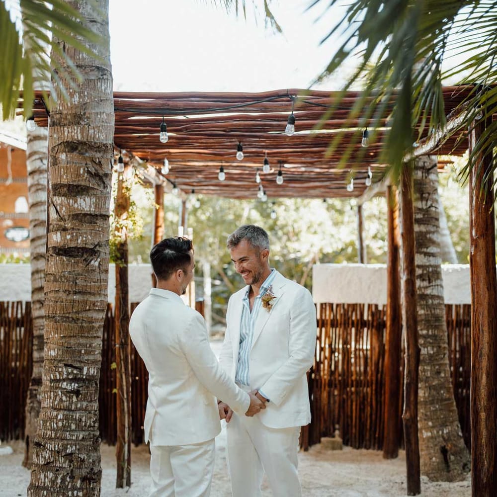 Grooms in complimenting white double breasted wedding suits on Holbox beach at destination LGBTQ+ wedding 