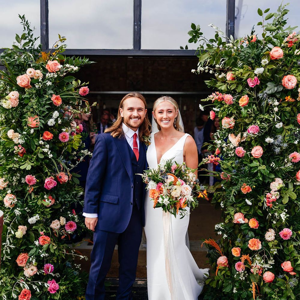 Colourful flower column arrangements with the groom wearing a blue three piece suit and bride in a Savin London wedding dress 