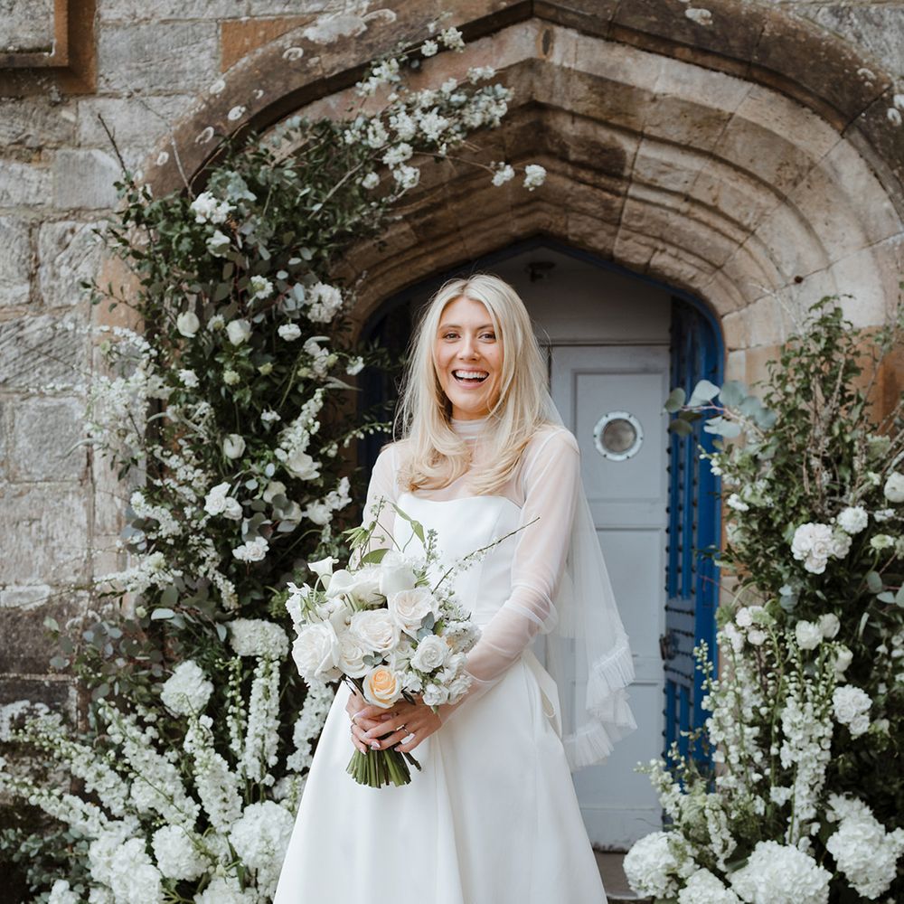 Bride in strapless wedding dress with mesh overlay top wearing ruffle veil carrying white bouquet 