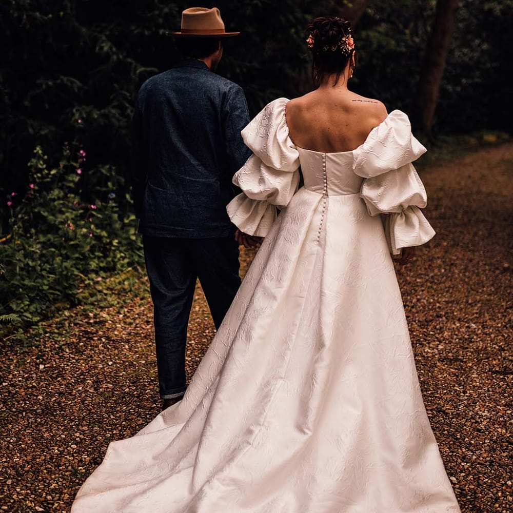 Bride in layered puff sleeve Jesus Peiro wedding dress walking hand in hand with the groom 