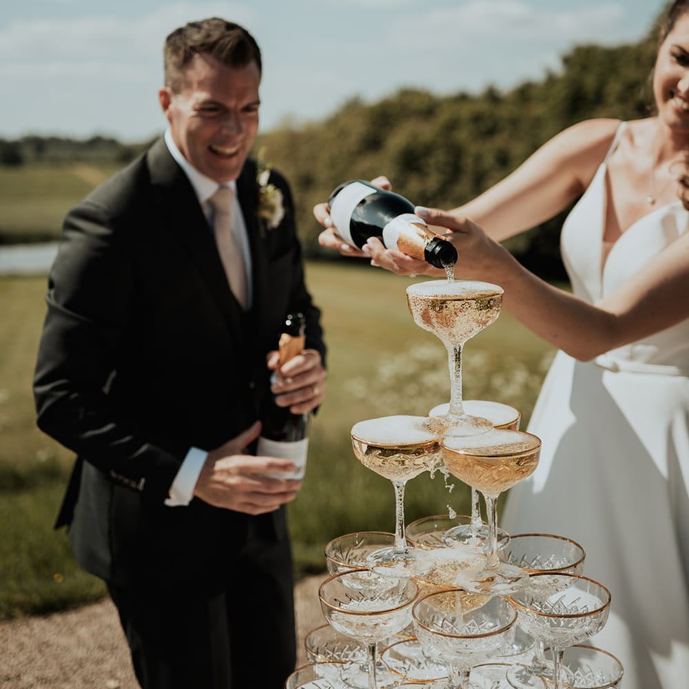 Bride pours champagne over champagne tower with gold rimmed coupe glasses 