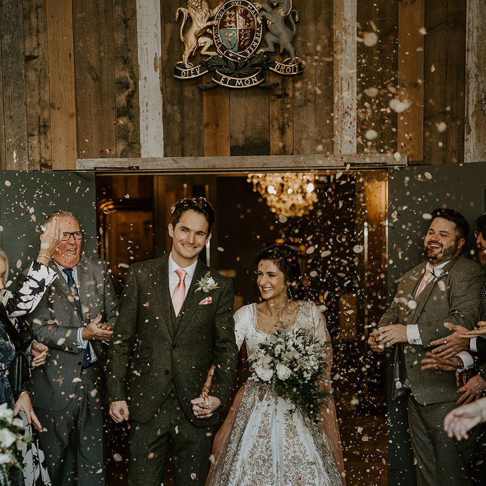 The bride and groom walk out of the ceremony together as the guests throw confetti 