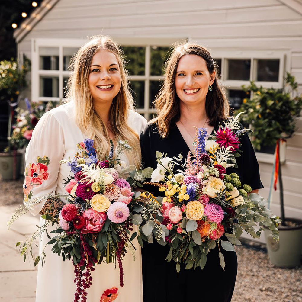 Bride in colourful embroidered wedding dress with bride in black wedding jumpsuit for same sex wedding day 