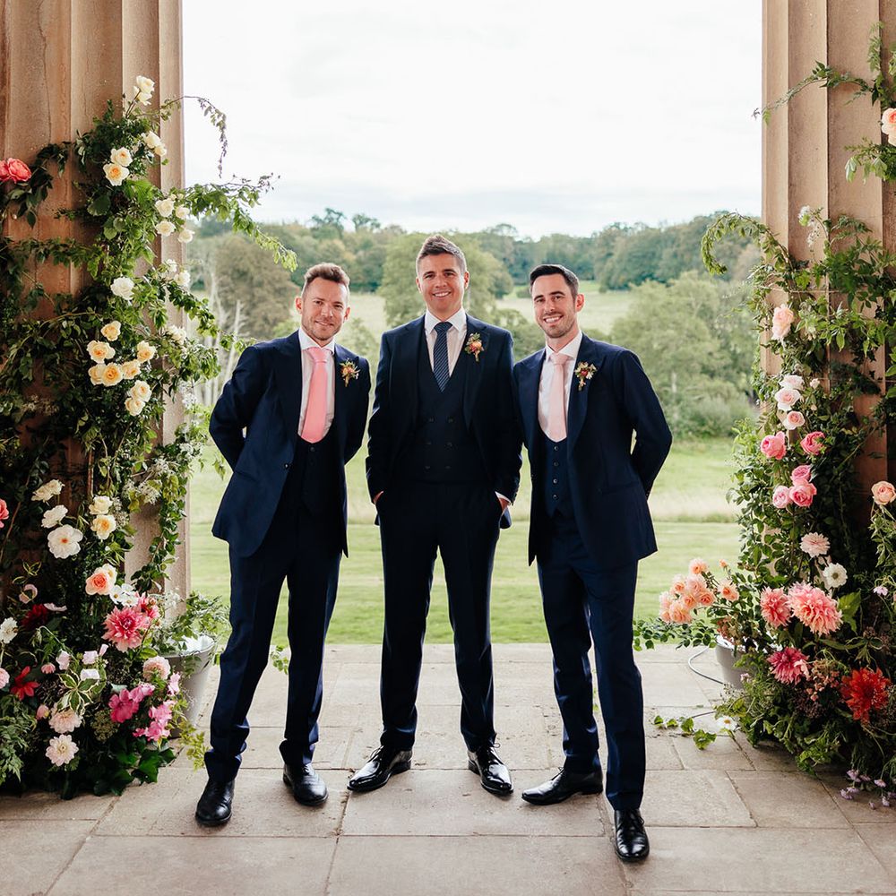 The groom and groomsmen in blue suits stand together waiting for the outdoor ceremony start