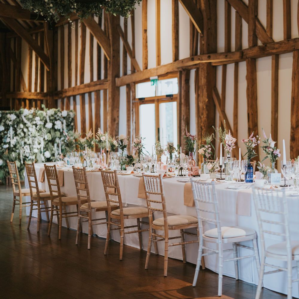 Wedding table featuring white tablecloth surrounded by white floral bouquets 