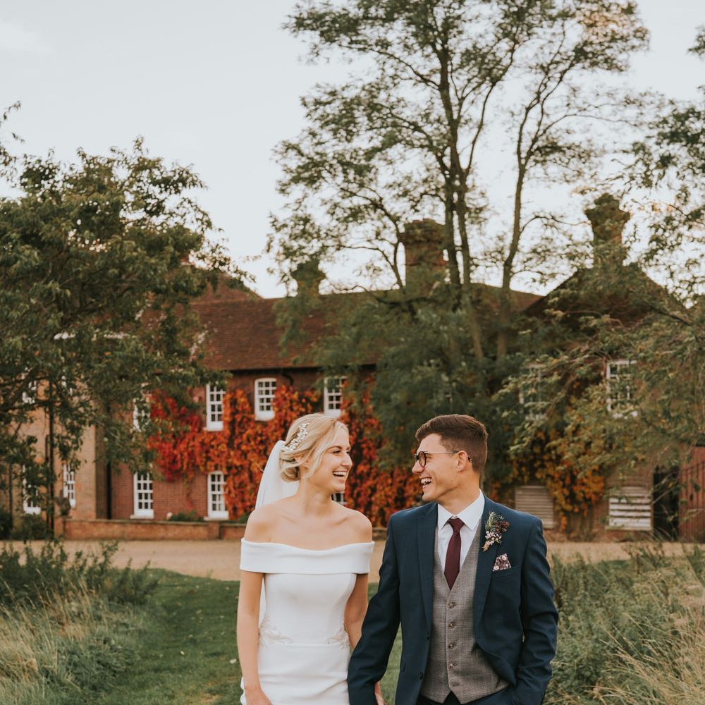 Bride & groom laugh together as they walk through the grounds of the venue