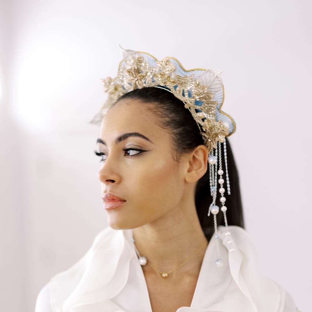 Bride looks to the side as she wears golden embroidered flower crown with peal embellishment falling to the side