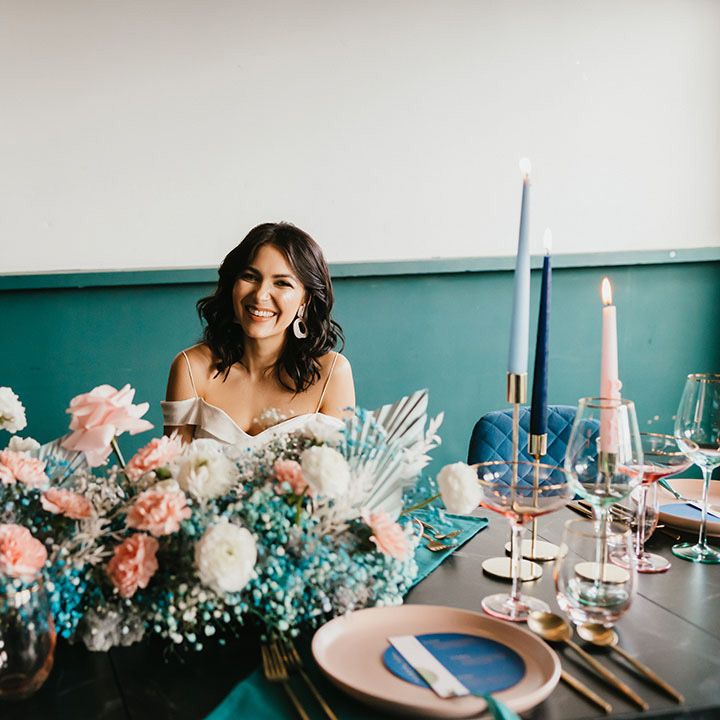 Bride sitting at the reception table with a teal blue gypsophila flower cloud with pink roses and dried palm leaves centrepiece 