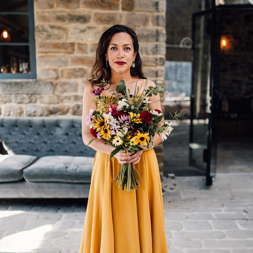 Bride wears yellow wedding dress and holds colourful bouquet