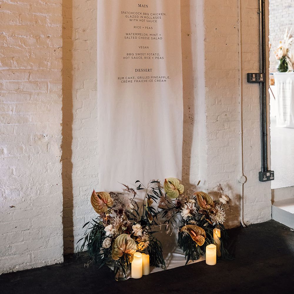 Large hanging fabric menu sign with flower arrangement at the footer 