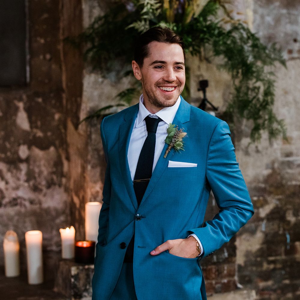 Dashing groom in blue suit and black tie with dried flower boutonnière and gold watch