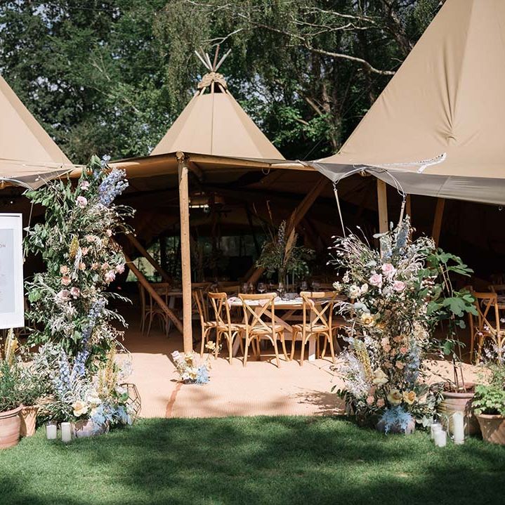 Buffalo tipi reception area with welcome wedding sign and large pastel flower displays with summer colours