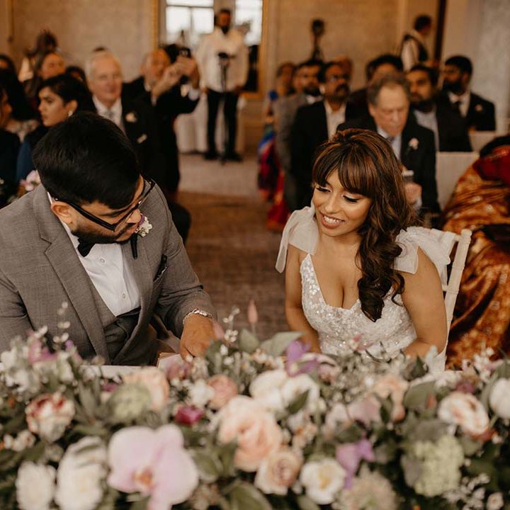 Bride and groom sitting at their wedding in front of large mixed neutral and green floral display 