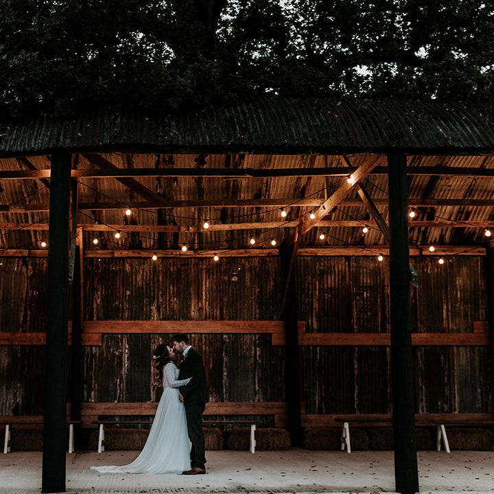 Bride and groom share a kiss under cosy lighting at rustic wedding venue, Silchester Farm based in Hampshire