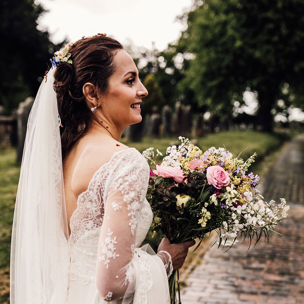 Bride with simple brown braid hairstyle with pink, yellow and purple wedding bouquet in lace wedding dress 