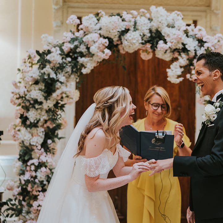 Bride and groom laugh as the bride puts on the groom's wedding ring 
