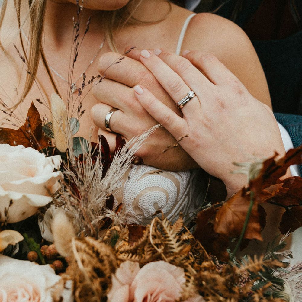 Bride wearing a silver wedding band and diamond engagement ring with groom wearing a plain silver wedding ring 