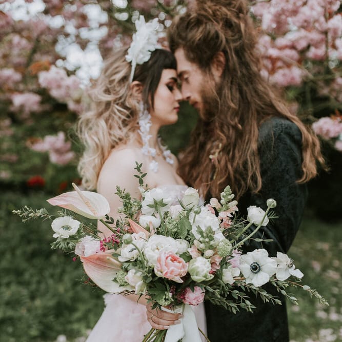 Couples' portrait under a blossom tree with bride holding a pink and white Spring wedding bouquet with anthuriums 
