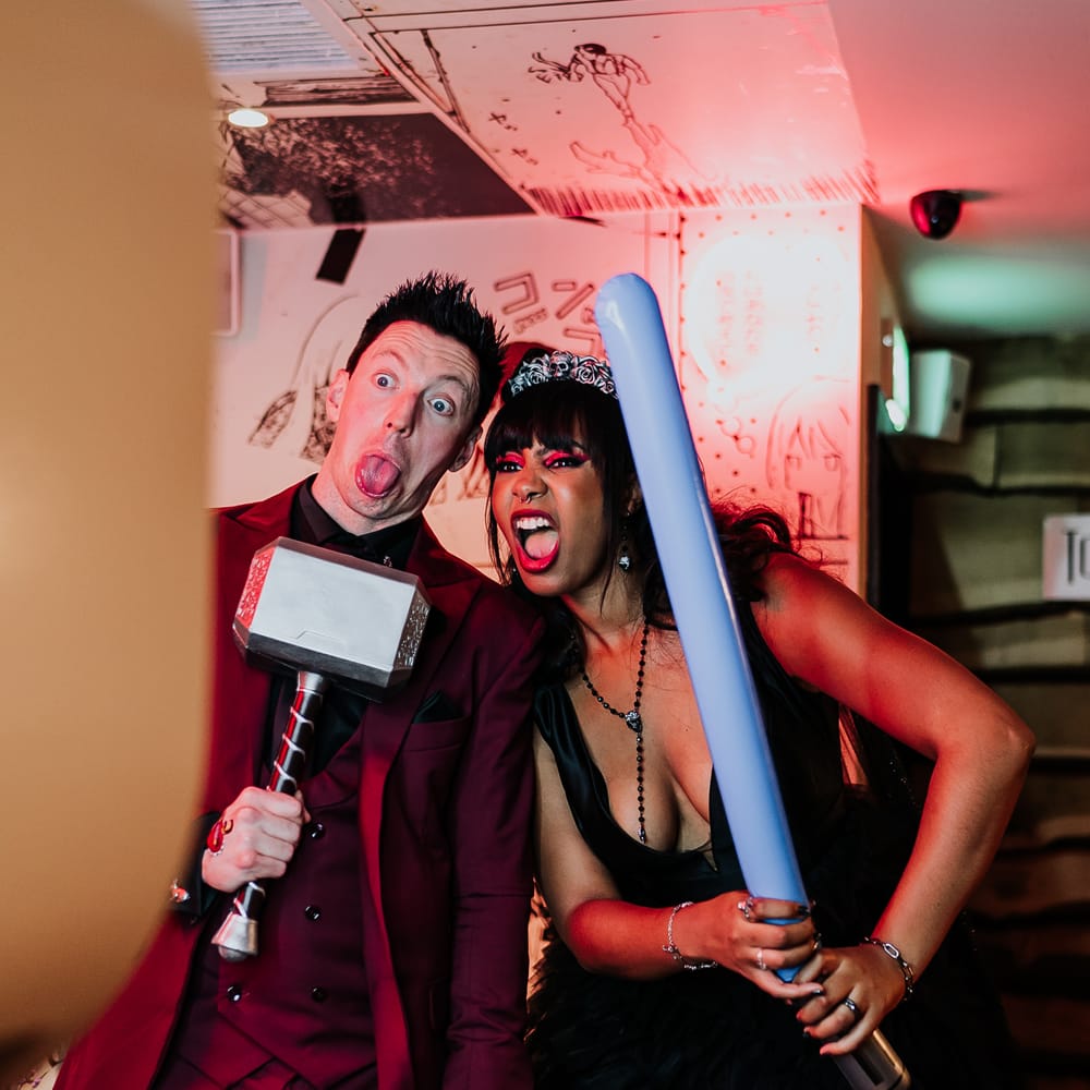 Bride & groom hold Thor hammer and lightsaber for photo booth wedding entertainment 