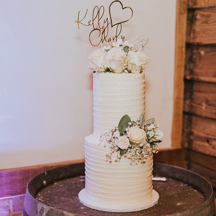 Two tier white rustic wedding cake with a personalised gold wedding cake topper and white rose and gypsophila decorations
