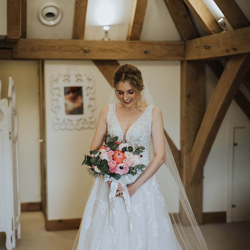 Bride holding a pink and white wedding bouquet with roses and peonies in a flower lace wedding dress