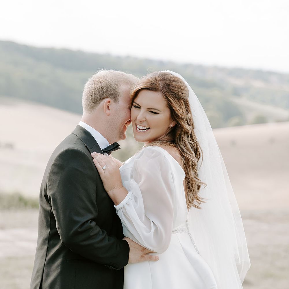 Bride in cathedral veil and sheer full sleeved wedding dress embrace outdoors for couples portraits