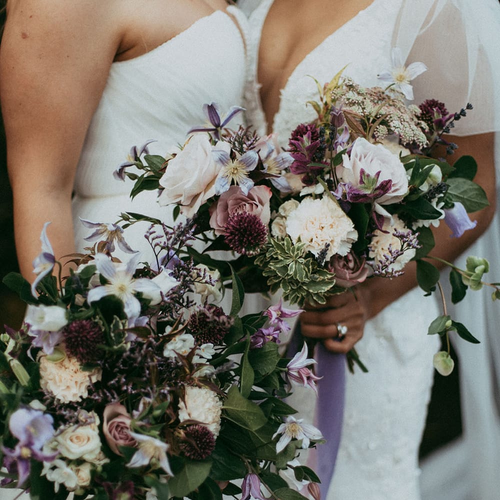 Matching bridal bouquets with white carnations, purple tulips, roses and foliage and lavender and white lace ribbon