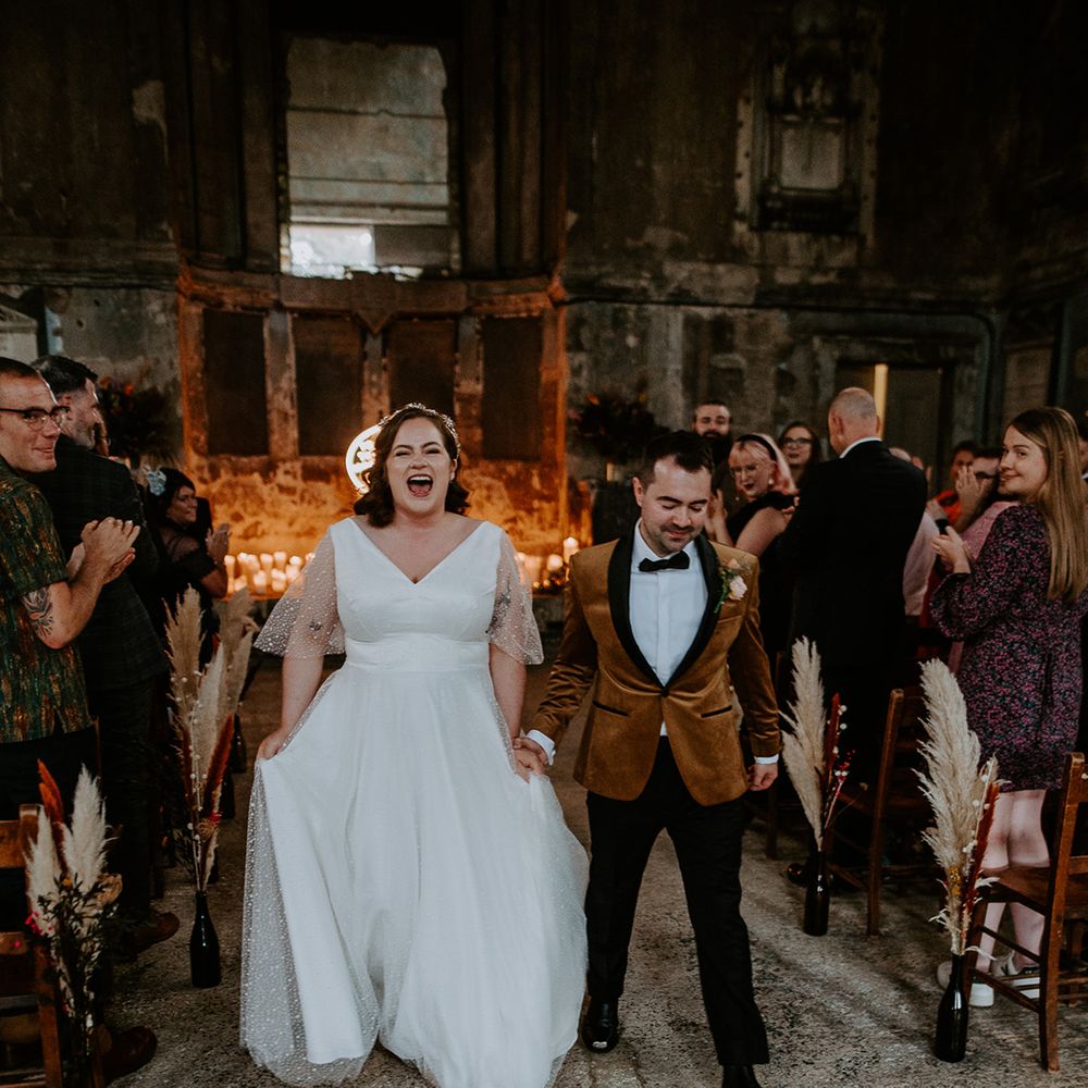 Bride and Groom walk up the aisle in coloured suit jacket and starry wedding dress