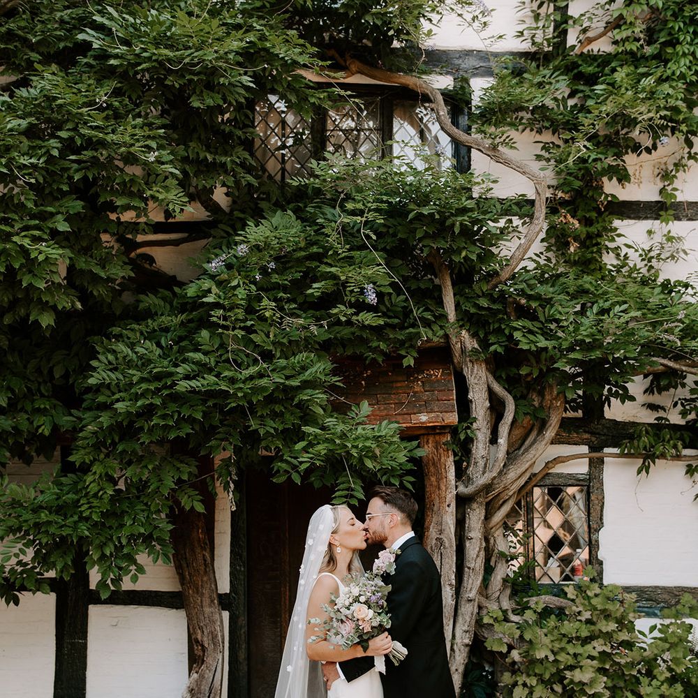 Bride in flower applique veil and simple wedding dress kisses the groom in three piece morning suit 