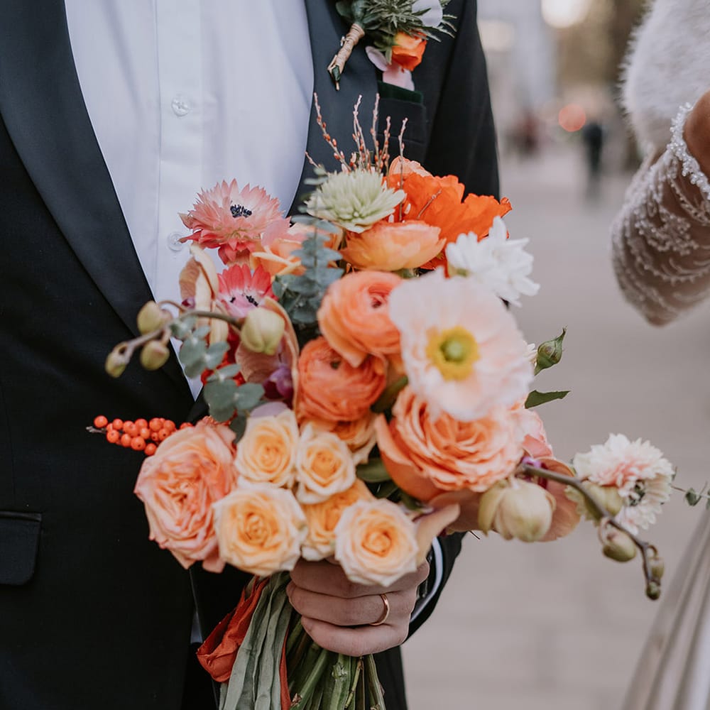 Bridal bouquet with light pink poppies, orange garden roses, eucalyptus, Christmas red berry garlands, dried flowers and sage green and orange ribbon