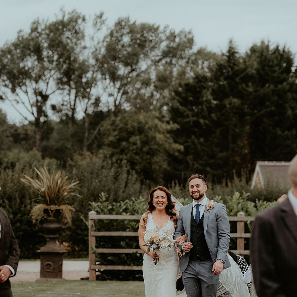 Bride is walked down the aisle by a man in a three piece grey suit with a blue tie and black waistcoat 