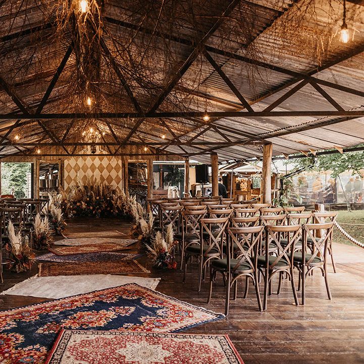Barn wedding ceremony with Moroccan rugs and dried floral arrangements lining the aisle alongside wooden chairs 