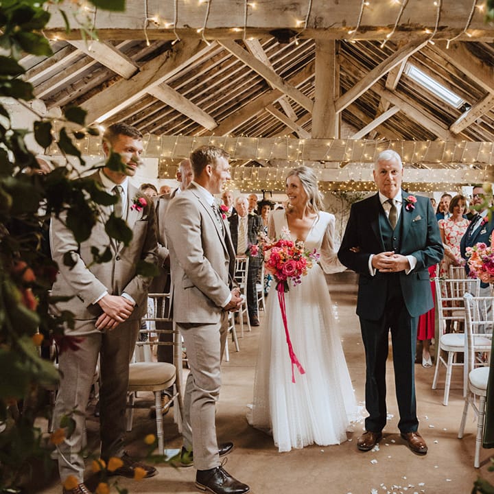 The father of the bride in a three piece navy suit walks the bride to the end of the aisle to meet the groom for their civil wedding ceremony 