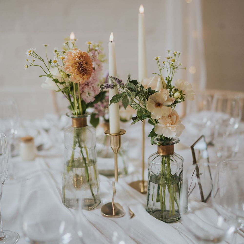 Glass bud vases with white candles in gold holders decorating the white tablescape with white tablecloth and table runner