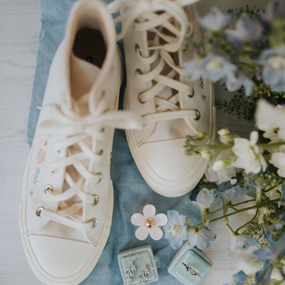Embroidered white wedding converse with blue fabric, blue velvet jewellery boxes with silver jewellery and white and blue wedding flowers 