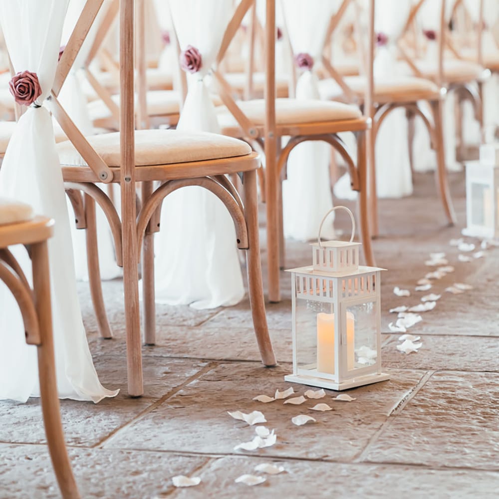 White wedding drapes tied with pink rose decorating the ceremony chairs with candles in lanterns and white rose petals 