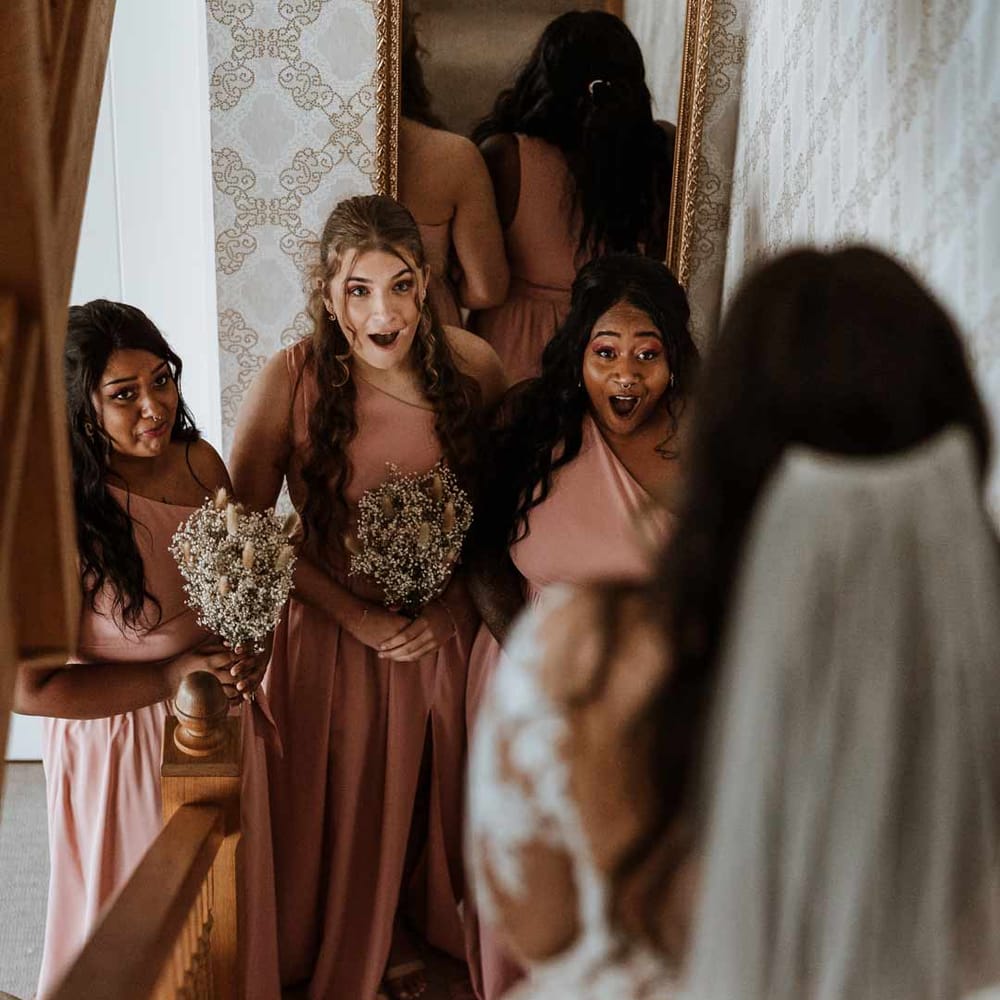 Bridesmaids in dusky pink one shoulder bridesmaids dresses holding dried flower bouquets seeing bride for the first time 