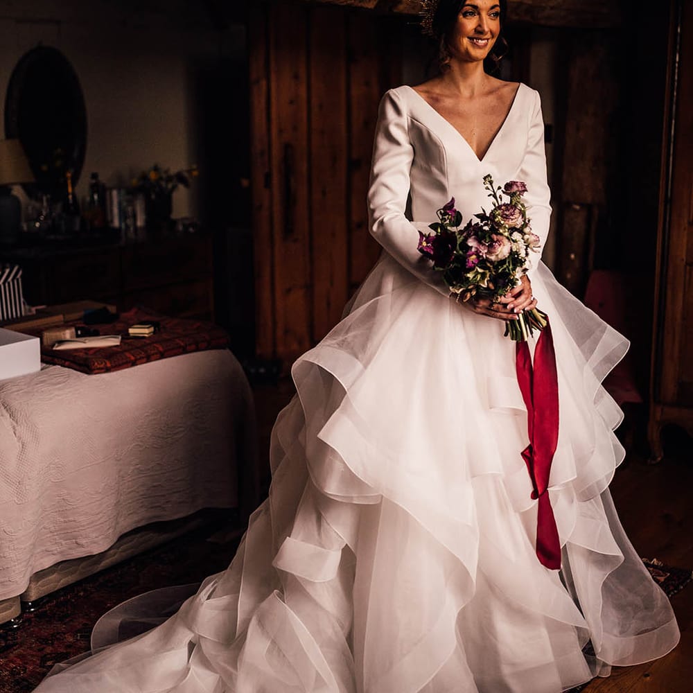 Bride in a layered ruffled wedding dress holding a dark pink winter bouquet tied with a red ribbon with gold crystal bride crown 